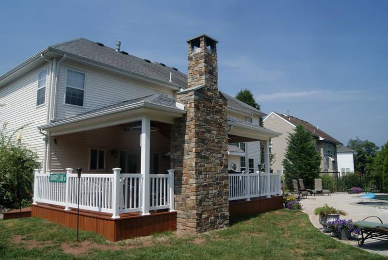 Backyard view of a two-story house with a wooden deck, a stone chimney, and a pool in the distance.