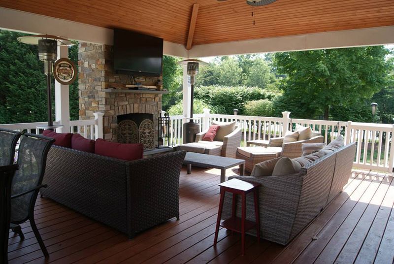 Covered outdoor patio with seating, fireplace, and TV overlooking a green landscape.