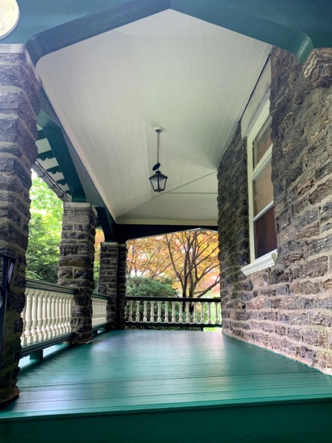 Covered porch with green floor and trim, stone pillars, white ceiling, and a view of trees.