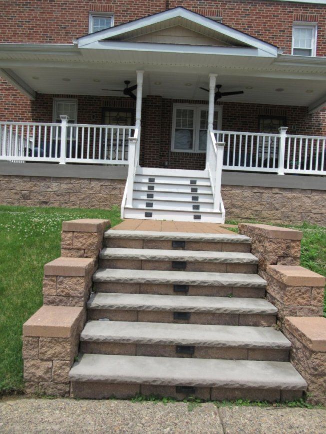 Brick house with steps leading up to a covered porch with white railing. Steps are made of stone.