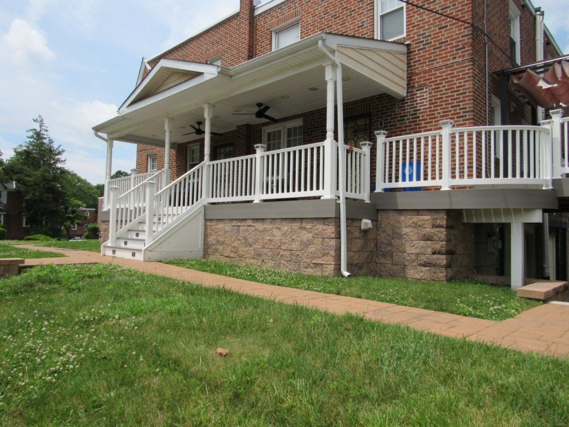 A brick house with a white porch and deck, and a green lawn in front.