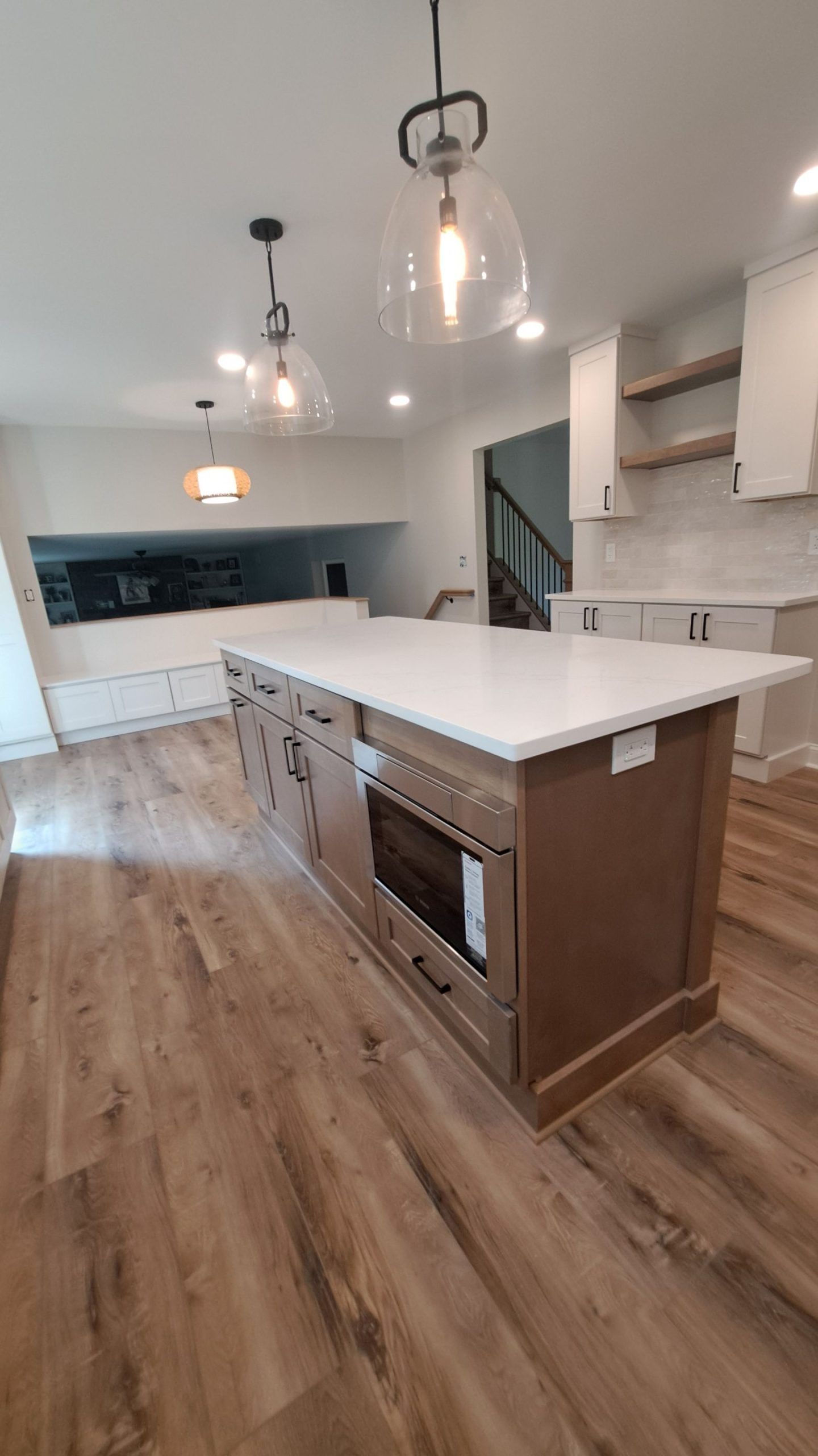 Kitchen with island, light-colored countertops, wood cabinets, and pendant lights. Hardwood flooring and white walls.