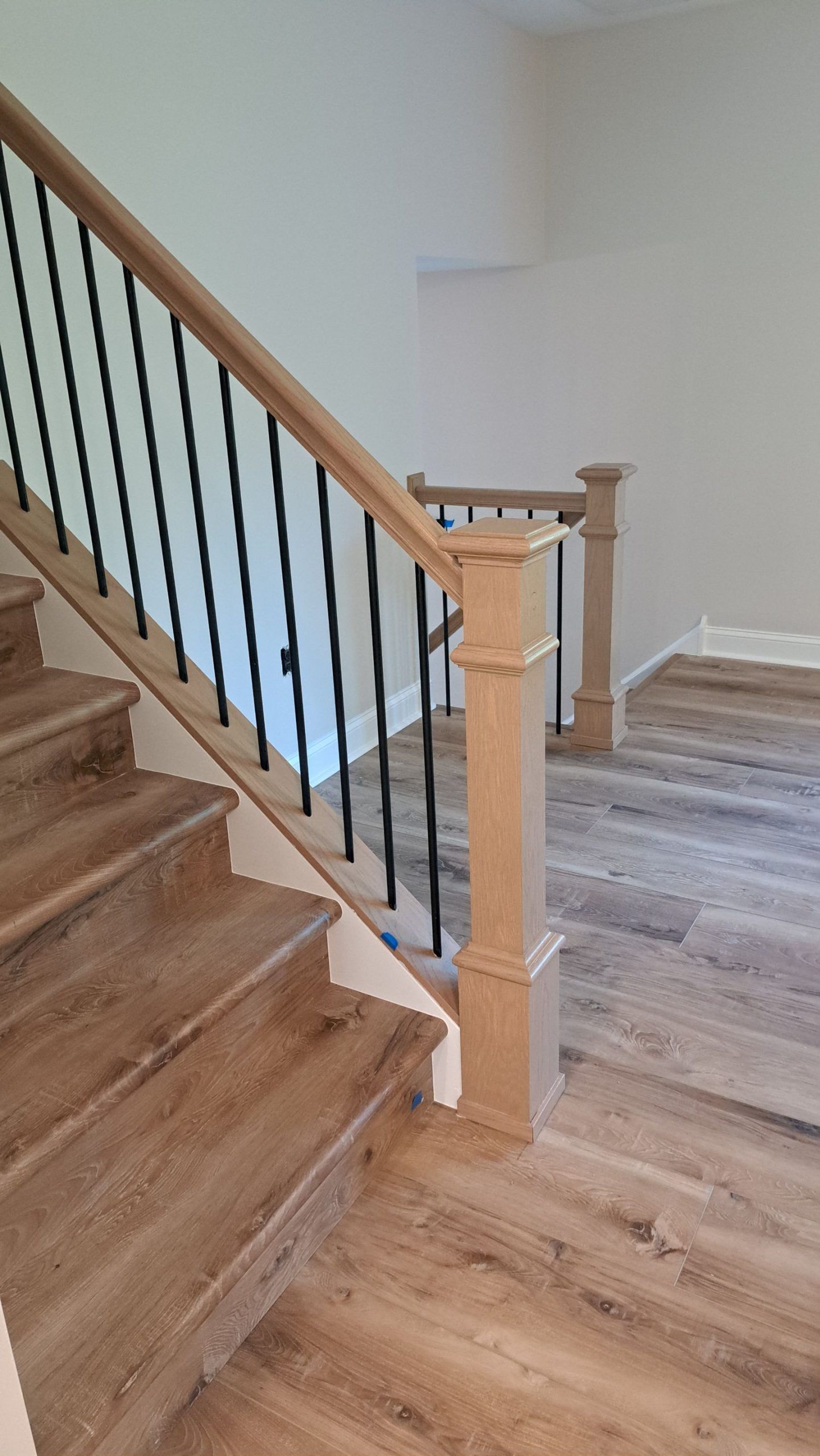 Wooden staircase with black metal balusters, leading up to a landing with similar flooring.