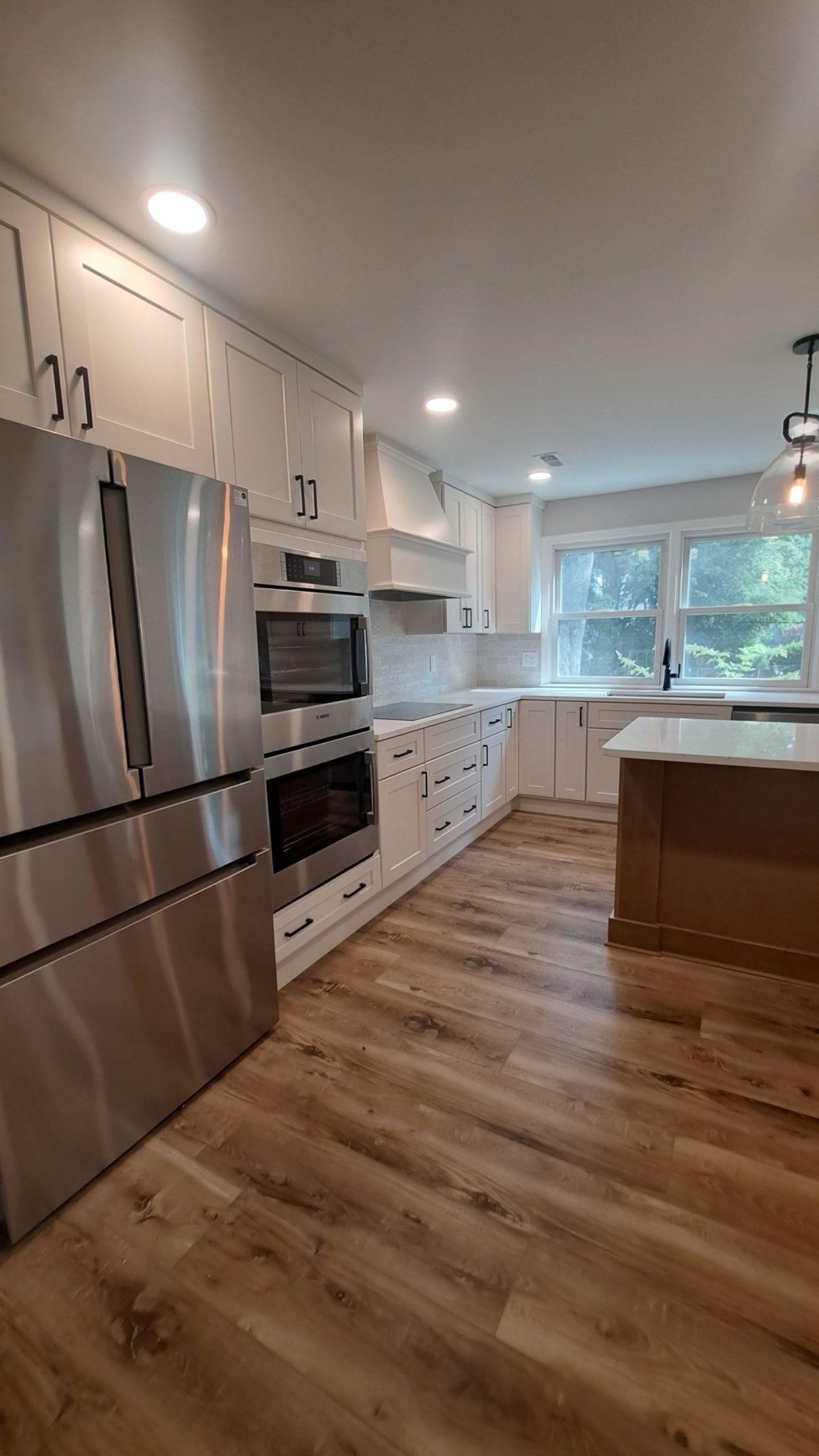 Modern kitchen with white cabinets, stainless steel appliances, and wood-look flooring.