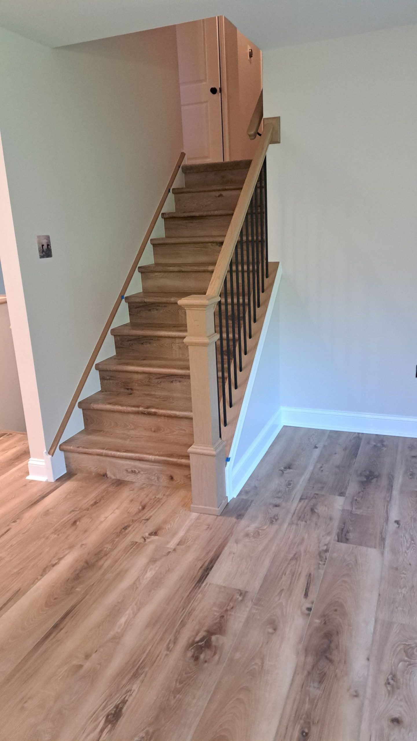 Wooden staircase with dark metal spindles and light-colored hardwood flooring.