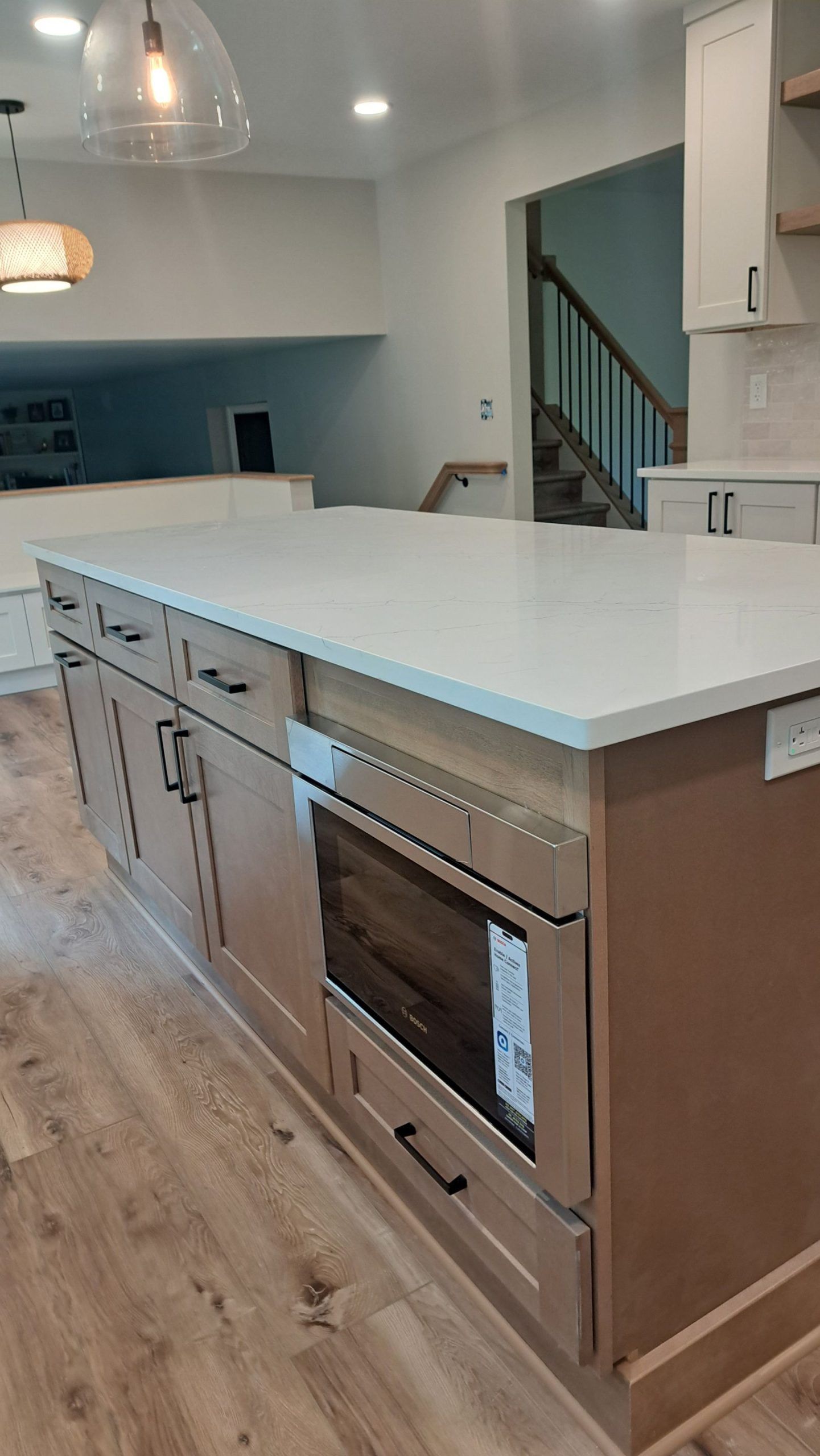 Kitchen island with built-in microwave, white countertop, tan cabinets, and wood-look flooring.