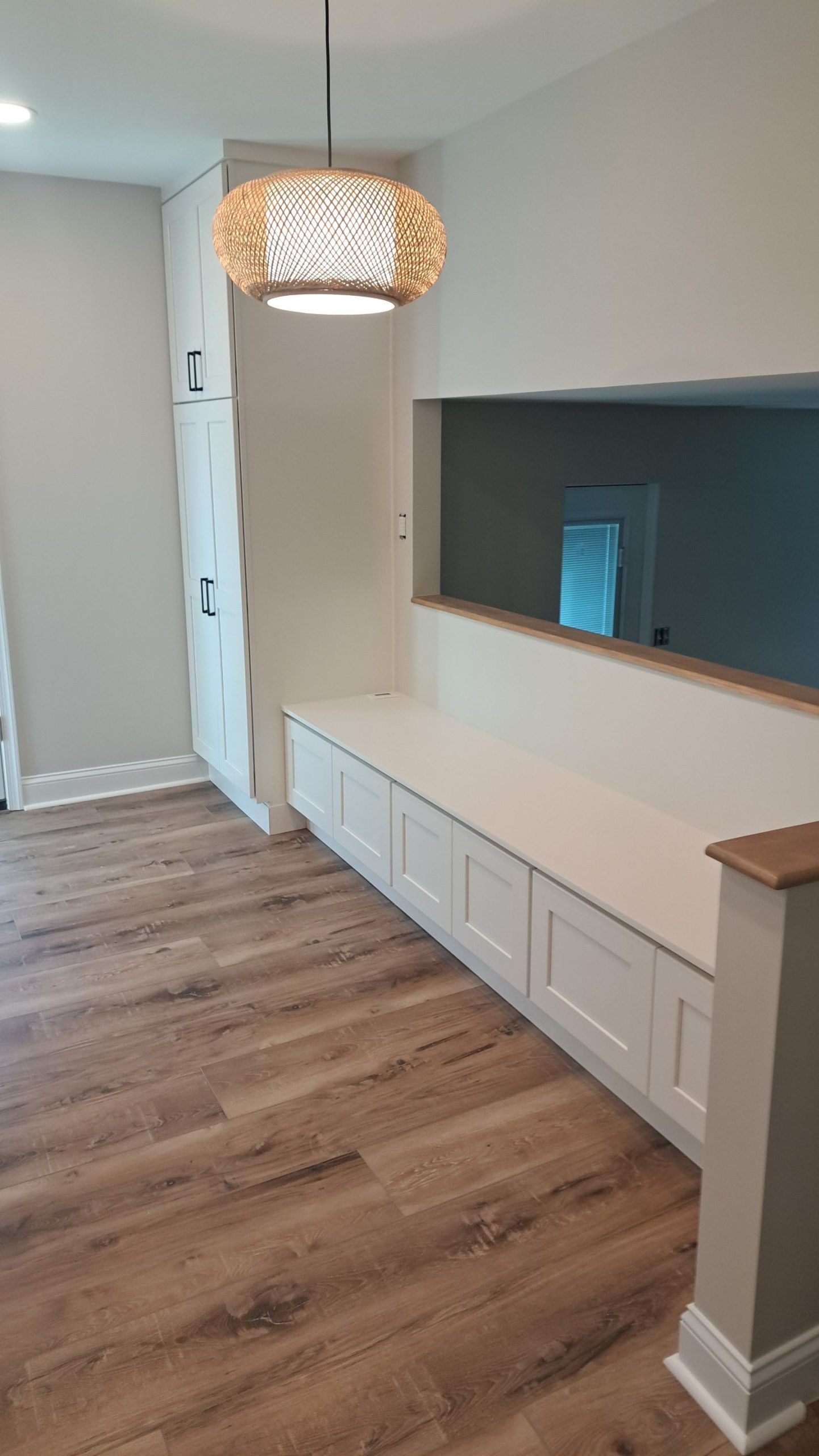 Built-in white storage bench with cabinets, hardwood floors, and pendant light in a home.
