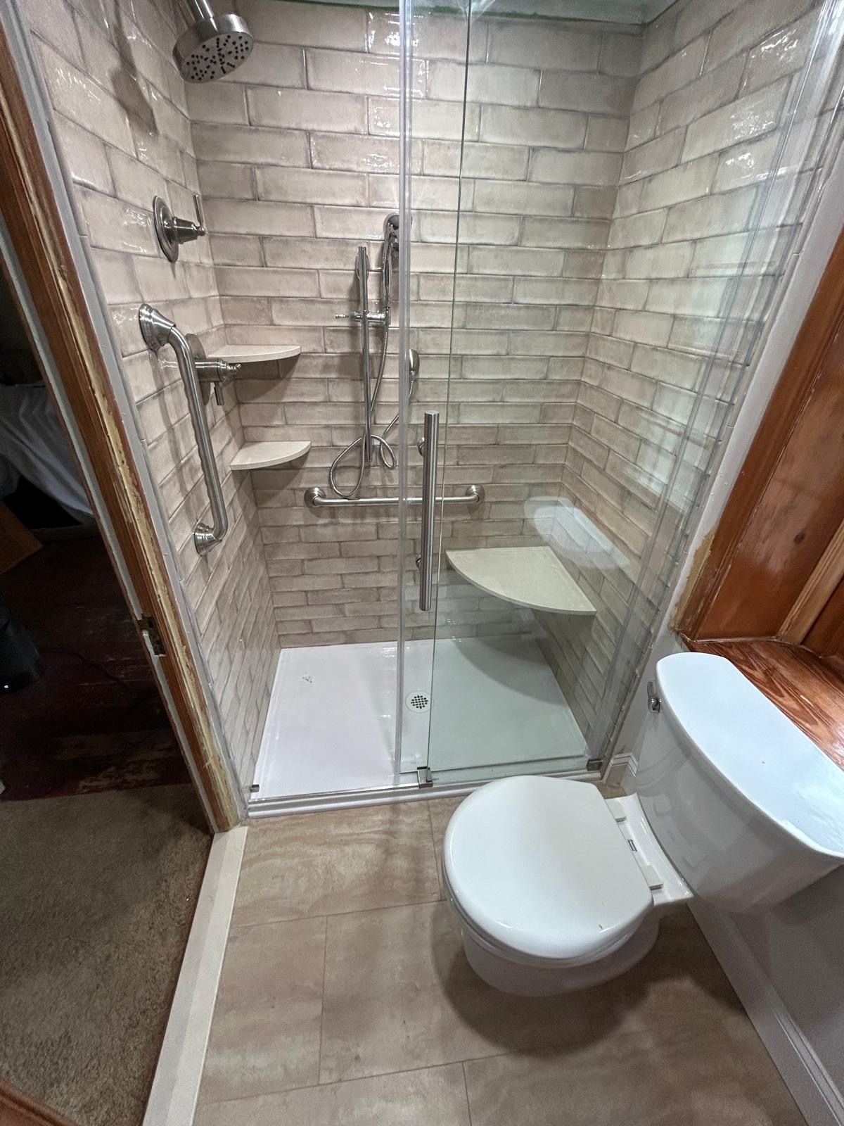 Accessible bathroom with shower and toilet, neutral-toned brick-style tiling, grab bars, and a shower seat.
