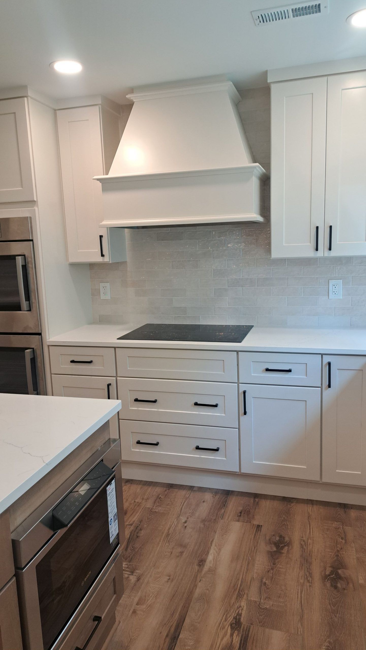 Modern white kitchen with light wood floors, cabinets, and appliances.