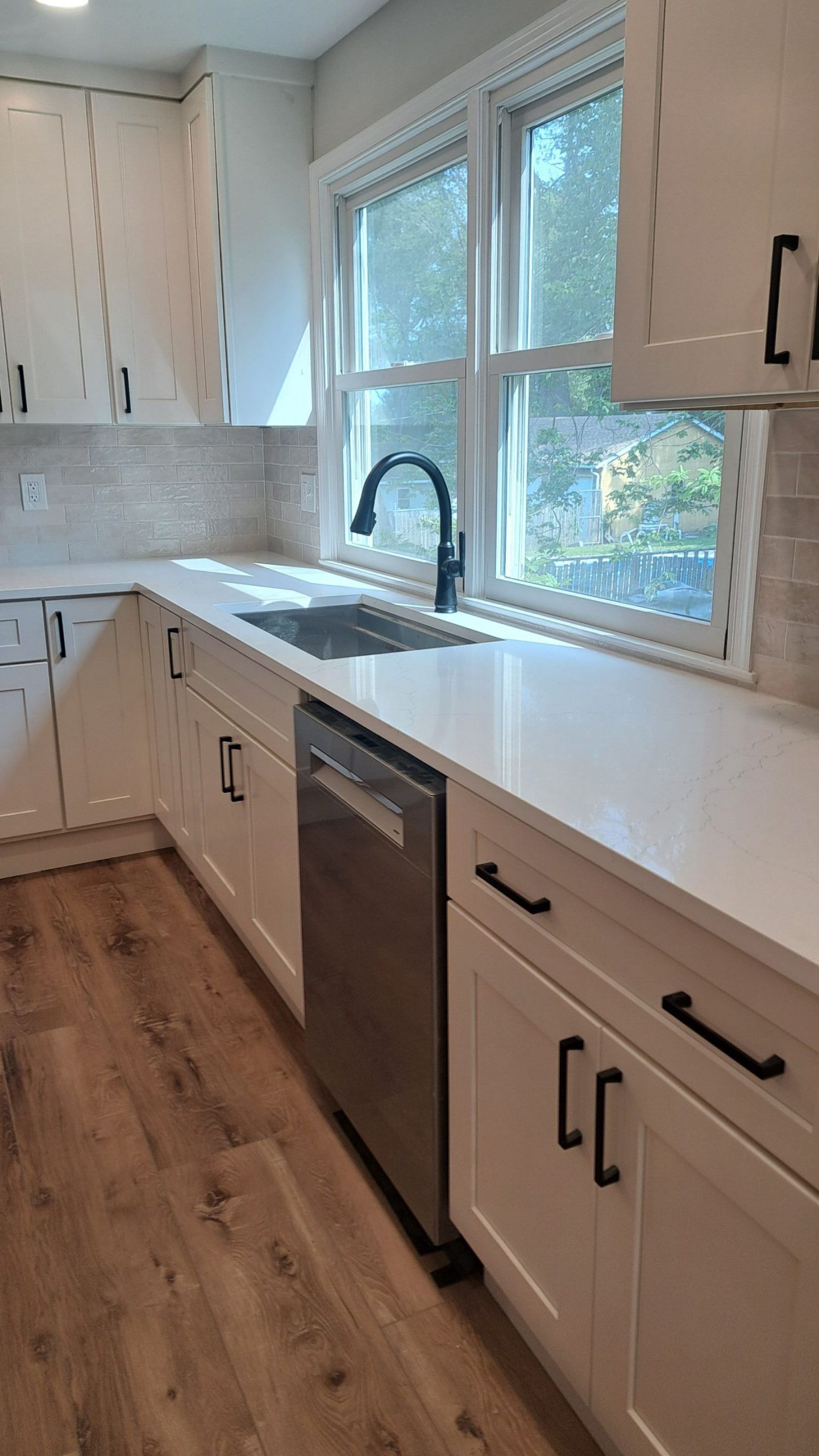 White kitchen with quartz countertops, stainless steel dishwasher, black hardware, and wood floors.