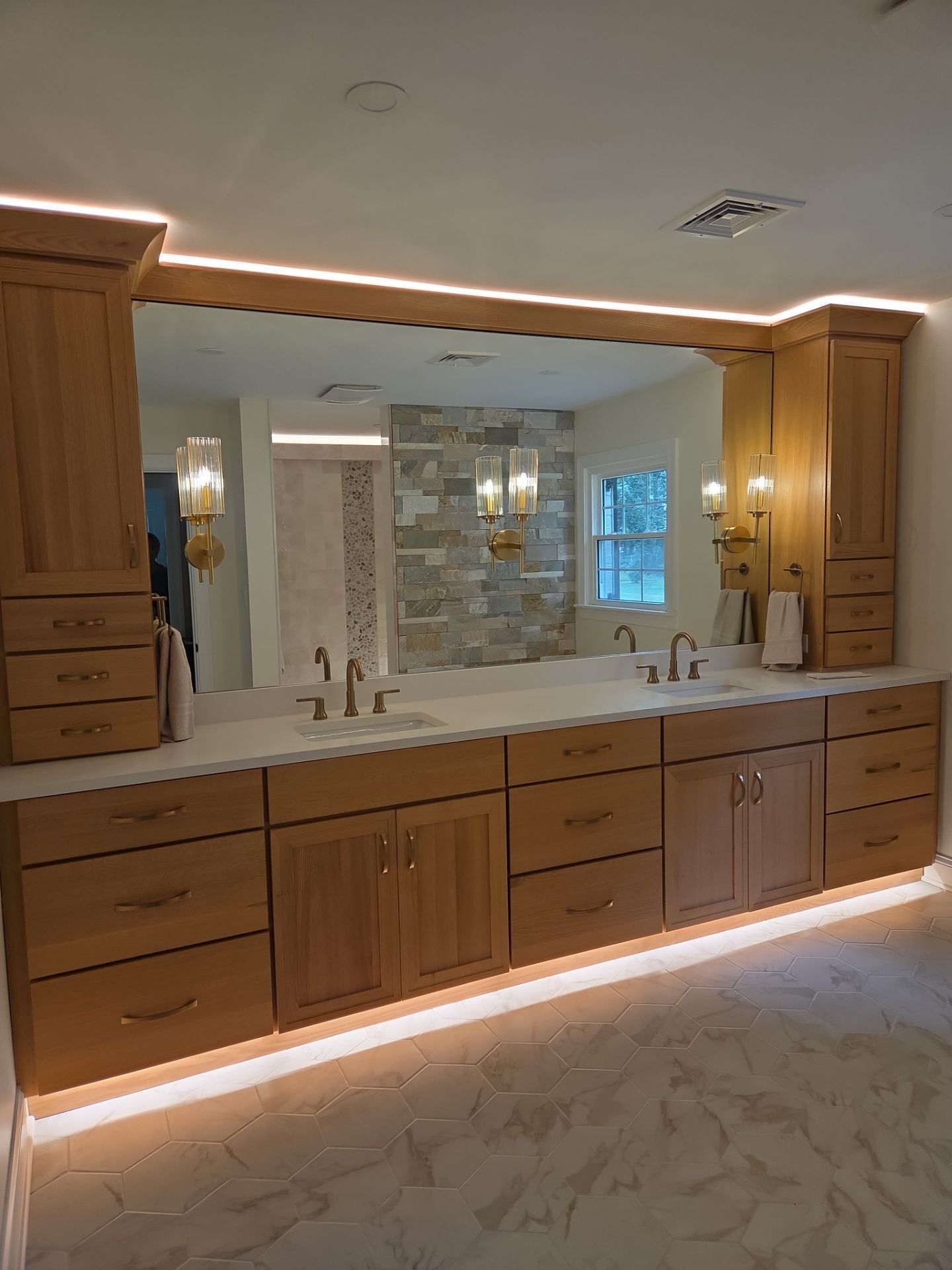 Bathroom vanity with light-colored wooden cabinets, marble countertop, large mirror, and recessed lighting.