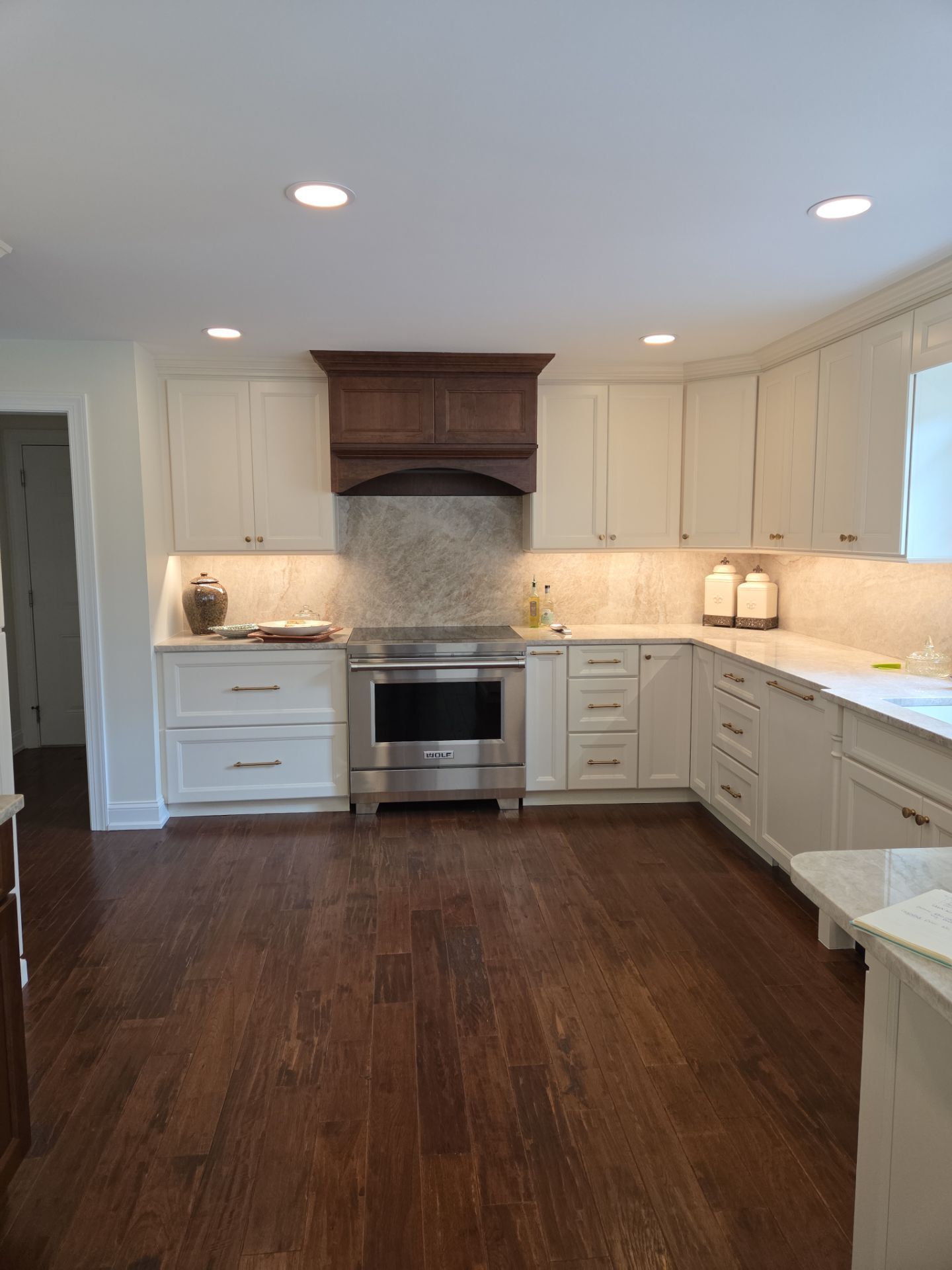 A kitchen with white cabinets, stainless steel appliances, dark wood floors, and a brown range hood.