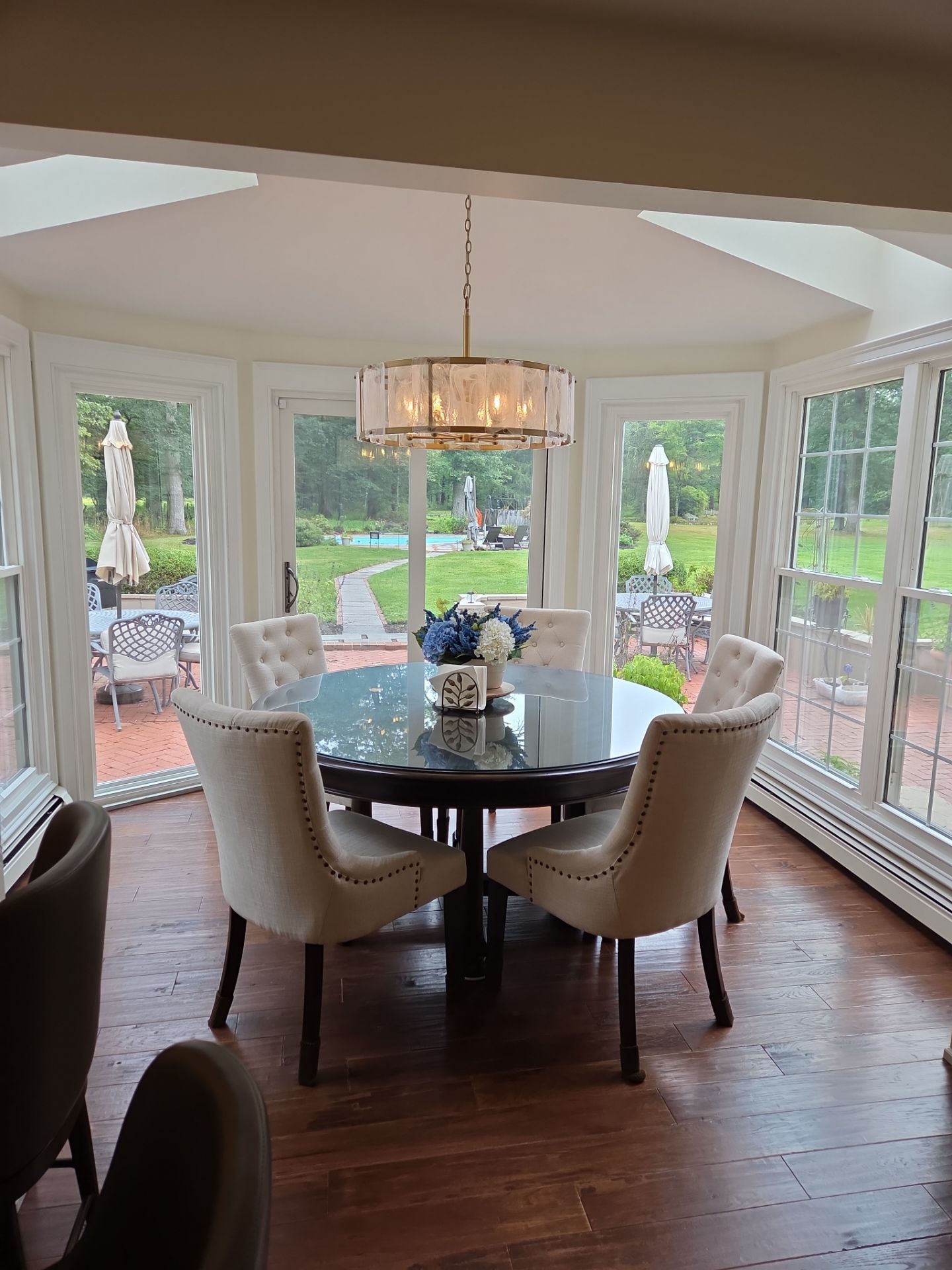Round dining table with six chairs, a chandelier, and windows overlooking a yard.
