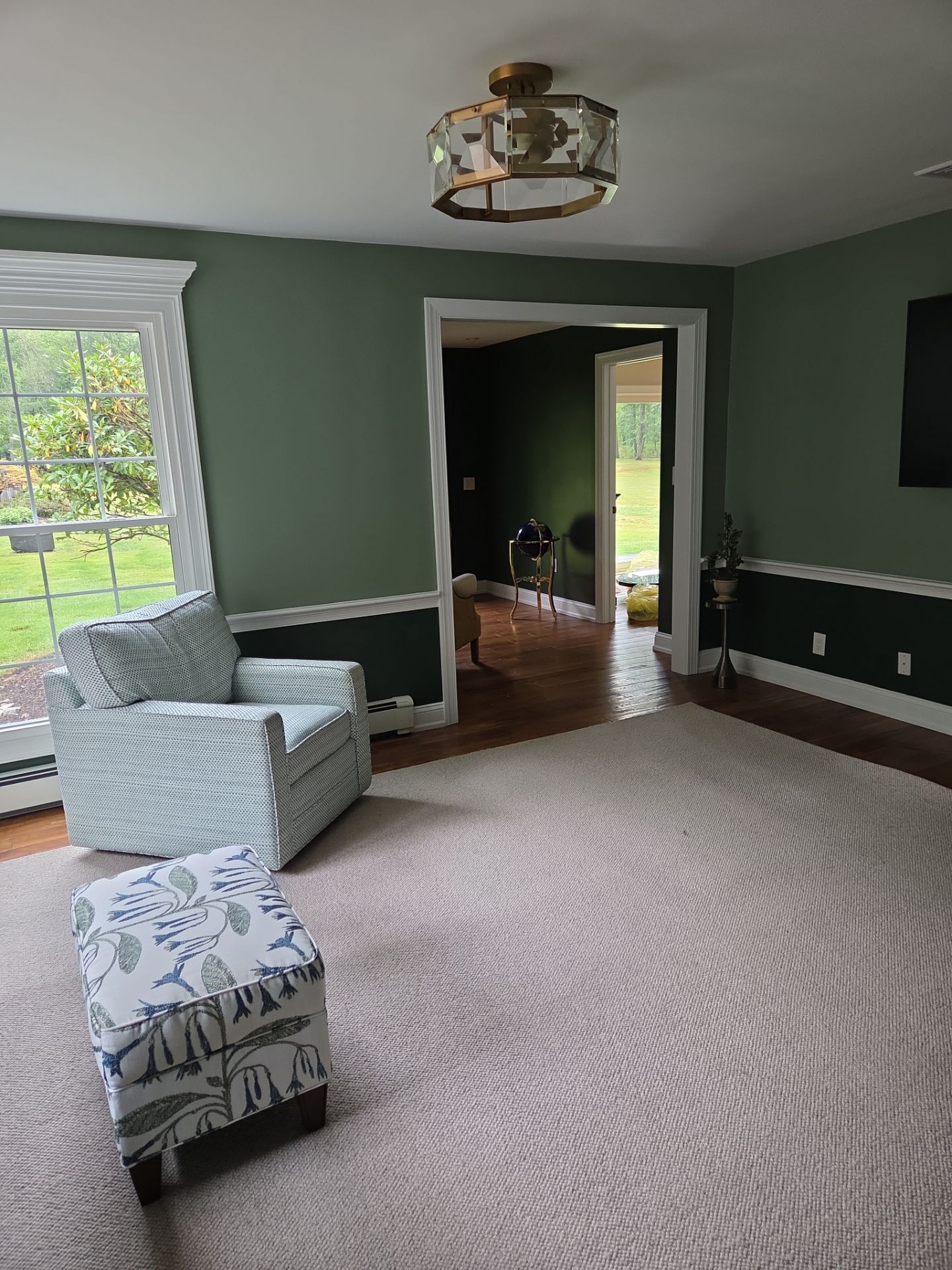 Living room with green walls, white trim, patterned armchair and ottoman on a beige rug.