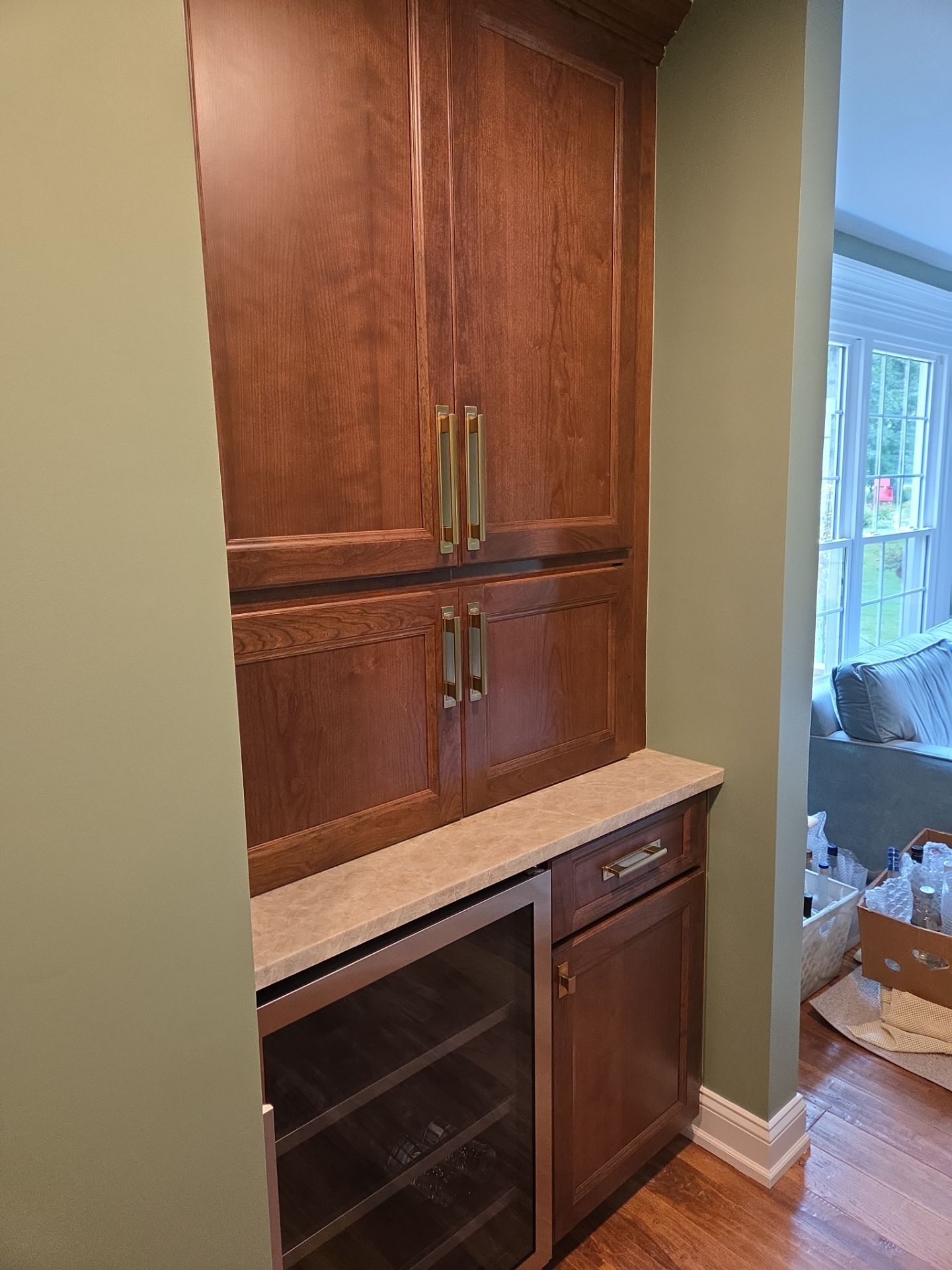 Built-in wooden cabinet with wine fridge, countertop, and hardware. Set between green walls.