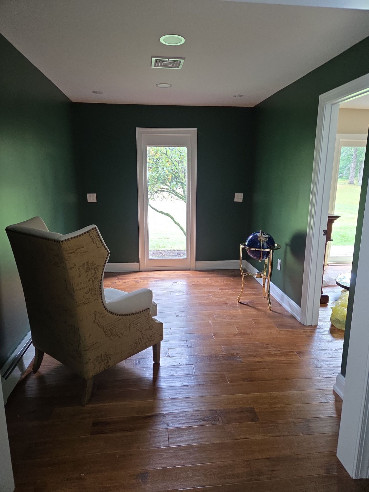 Cozy room with dark green walls, hardwood floors, a wingback chair, and an open doorway leading outside.