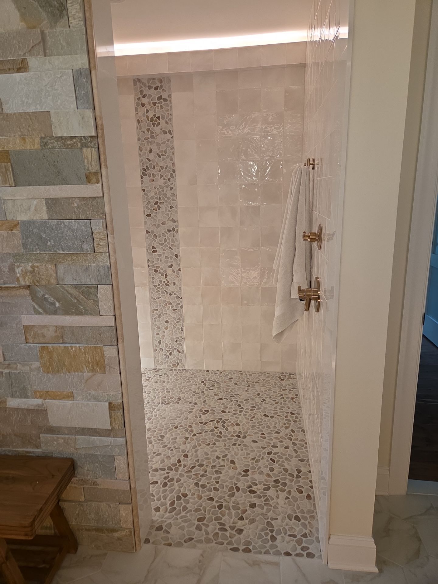 Shower with pebbled floor and light beige tile, glass door, and gold fixtures.