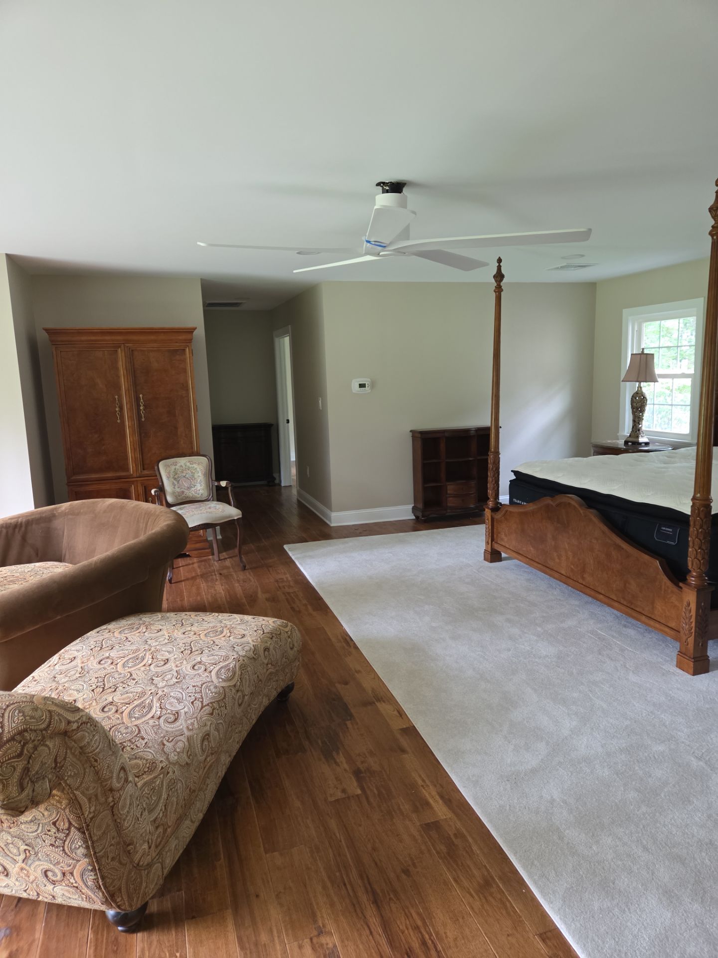 Spacious bedroom with hardwood floors, carpet, four-poster bed, chaise lounges, and armoire.
