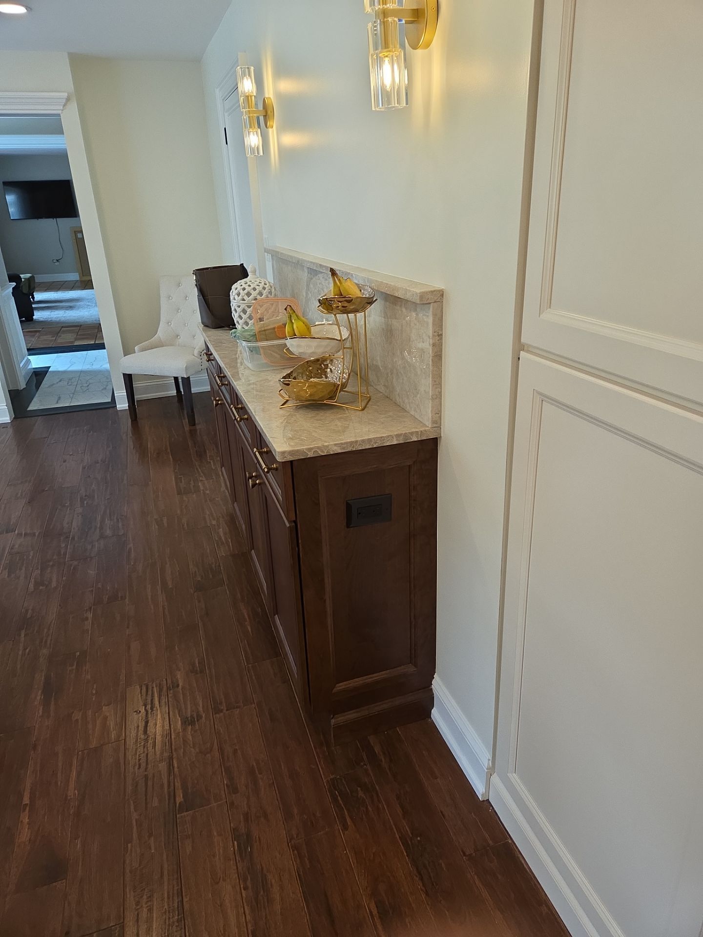 Dark wood cabinets with light countertop and wall sconces, next to a hallway with hardwood floor.