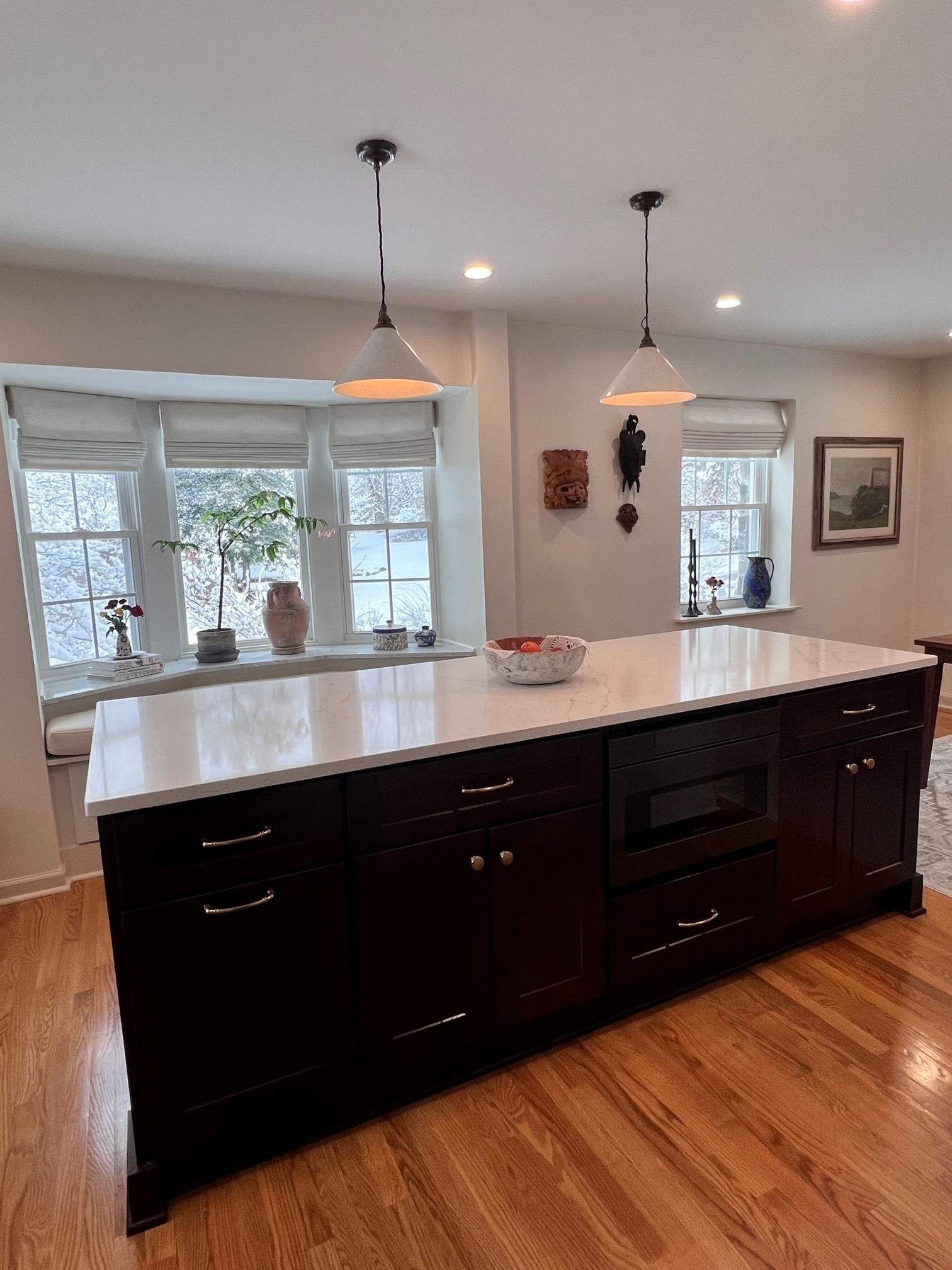 Kitchen island with white countertop, dark cabinets, pendant lights, and bay window.