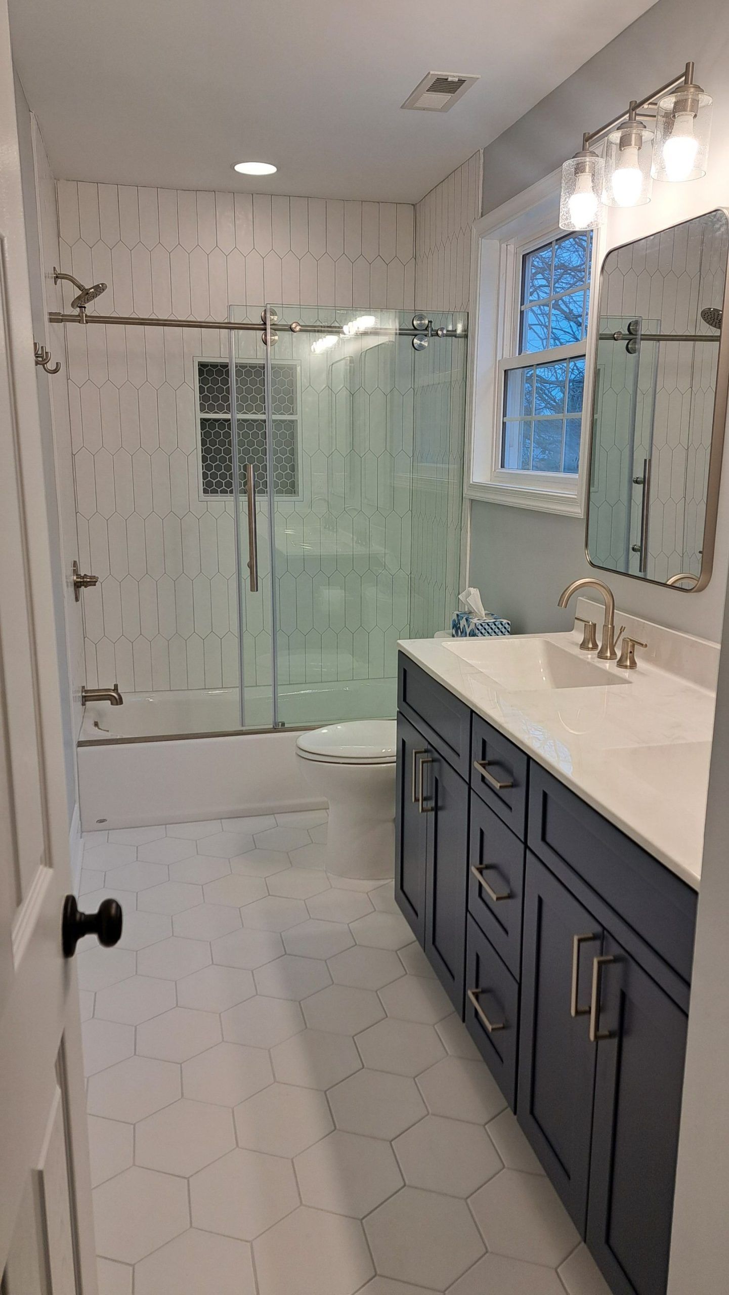 Bathroom with blue vanity, hexagon tile floor, and glass shower.