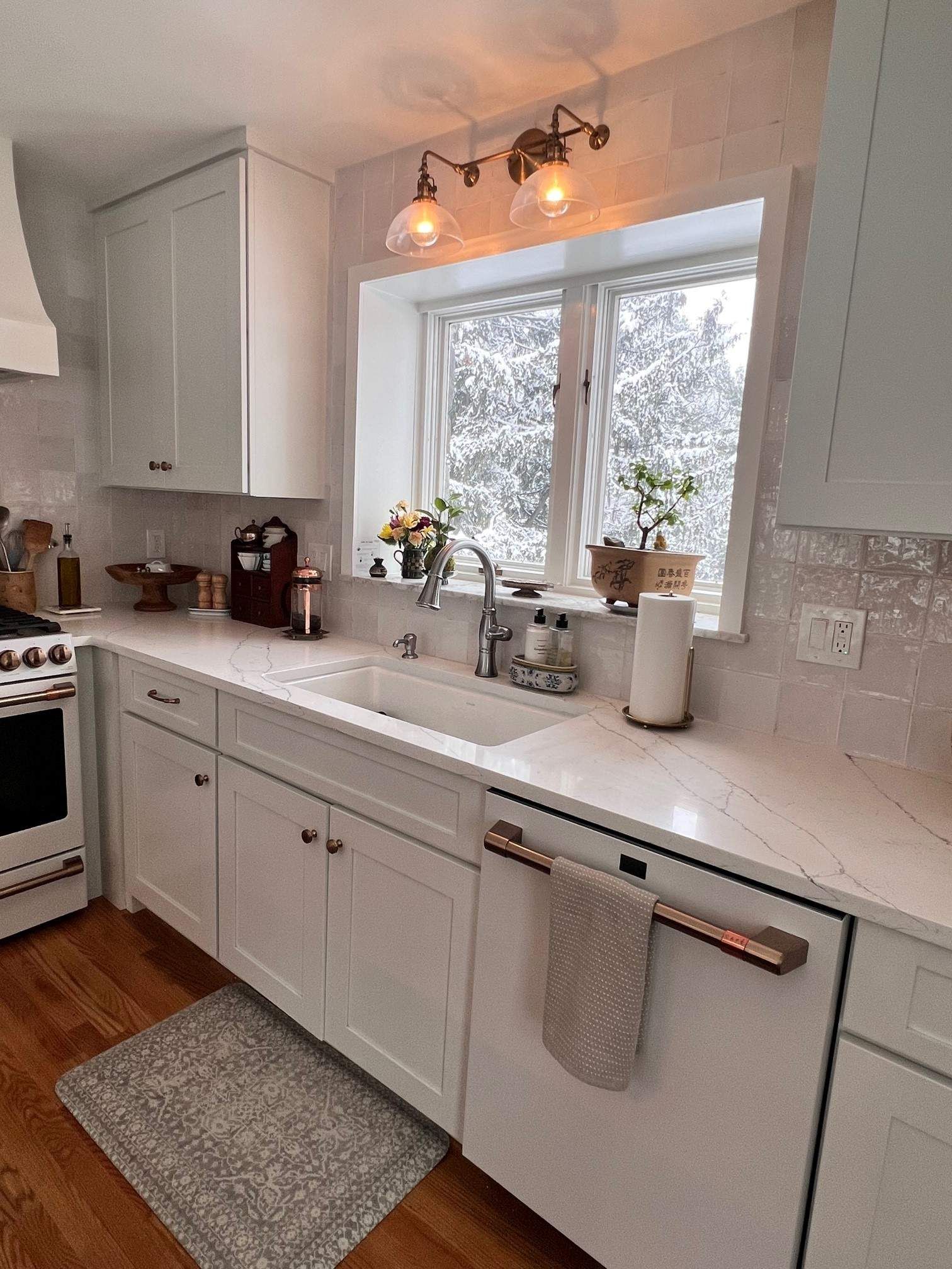 White kitchen with window overlooking a snowy landscape. White cabinets, countertops, and appliances.