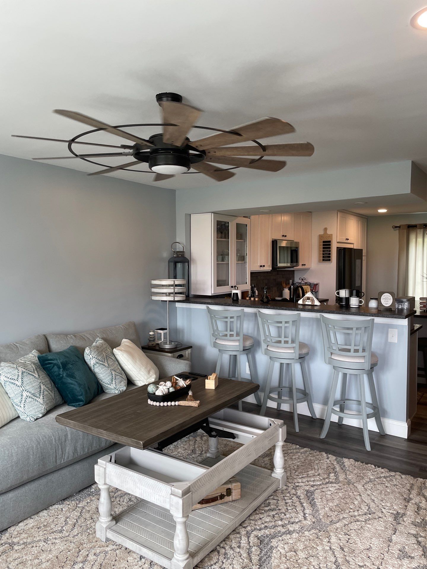 Living room with a gray sectional, bar stools, and a ceiling fan.