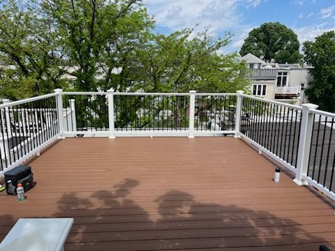 Wooden deck with white railings and black spindles, overlooking trees and buildings on a sunny day.