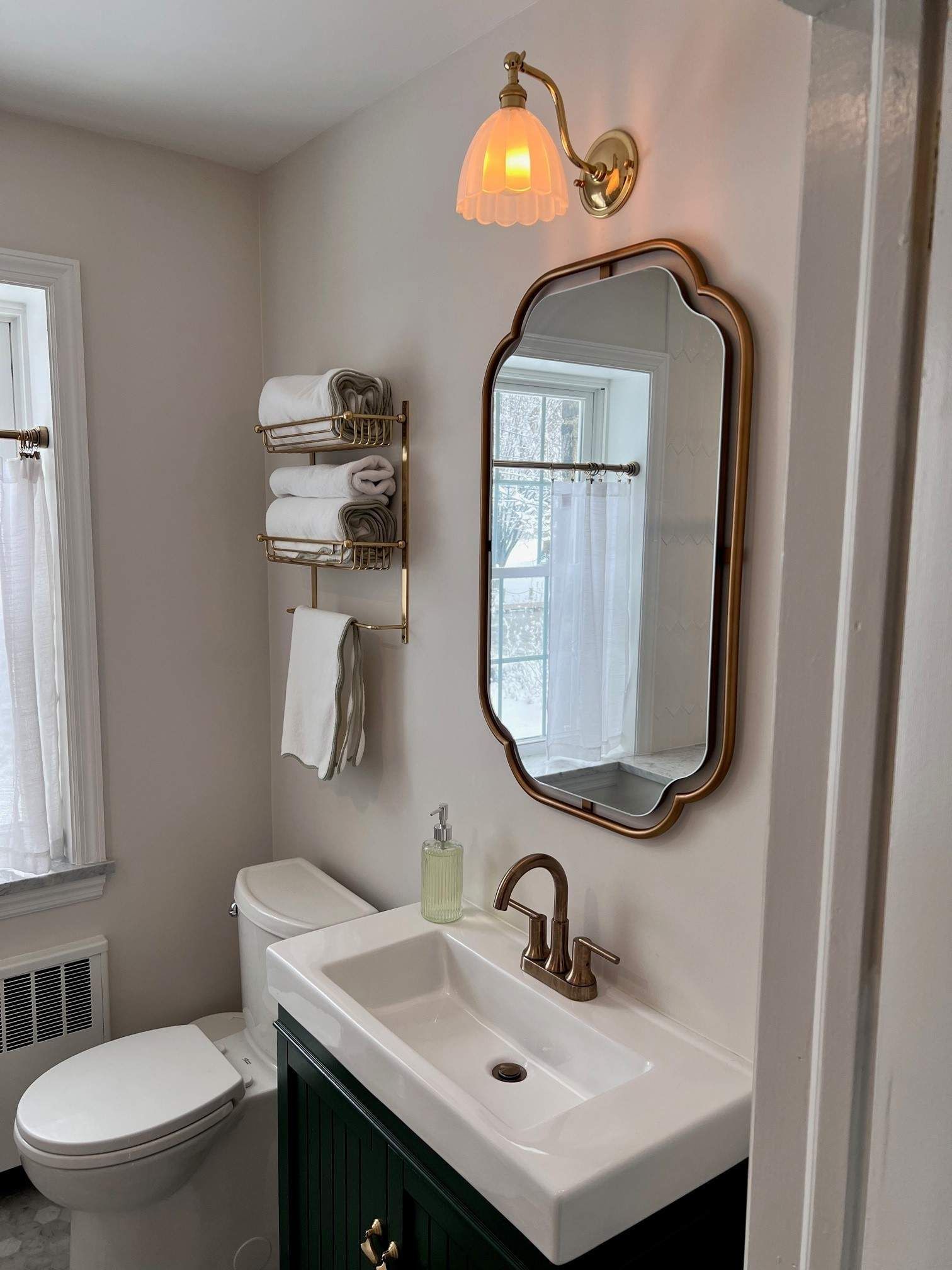 Bathroom with a gold-framed mirror, green vanity, and white sink. A gold towel rack and matching light fixture are also present.