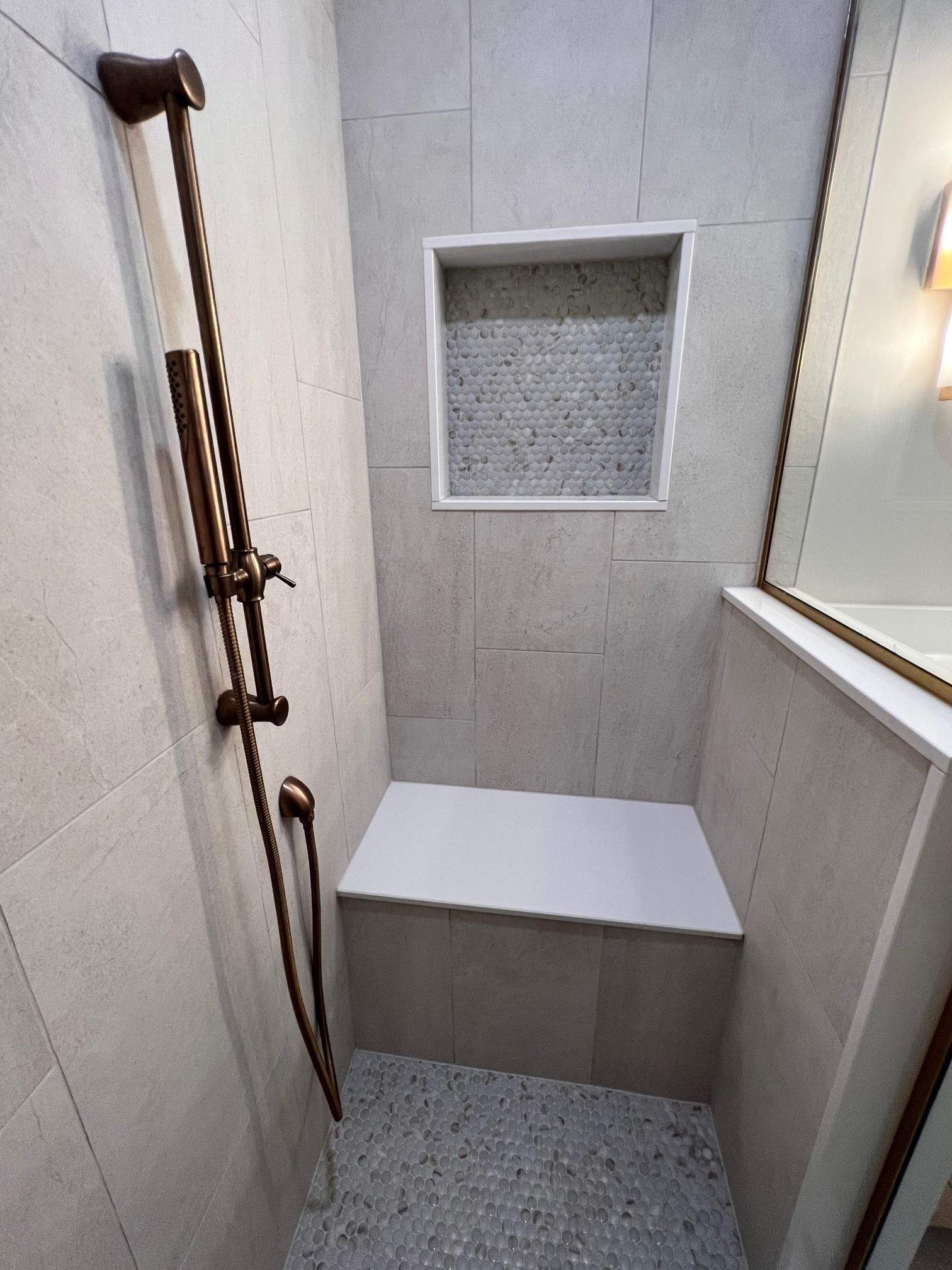 Bathroom shower with built-in bench and recessed shelf, light gray tile, bronze shower fixture.