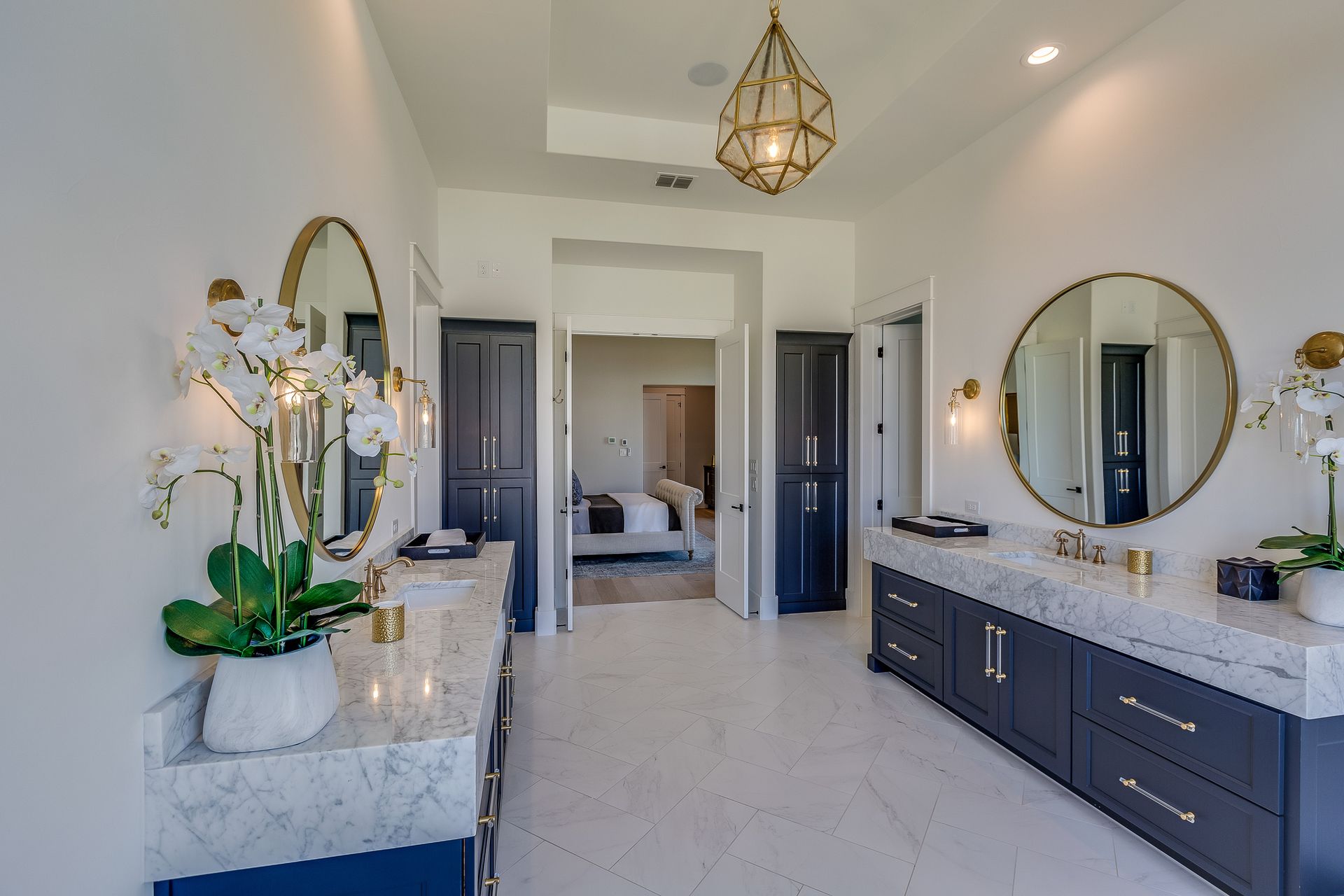 A luxurious master bathroom with white walls, navy cabinets, marble countertops, and gold accents.