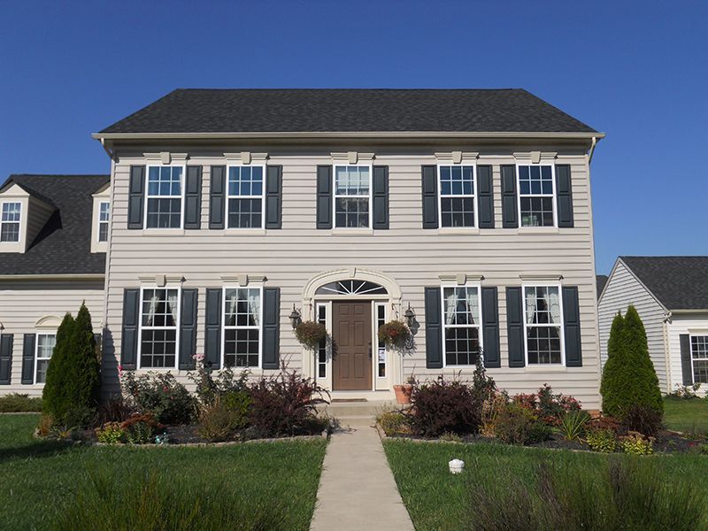 Two-story house with beige siding, black shutters, and a walkway leading to a brown door; blue sky background.