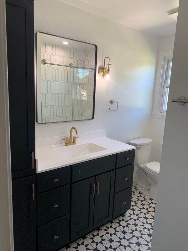 Dark green bathroom vanity with gold hardware, white countertop, black and white patterned tile, and patterned mirror.