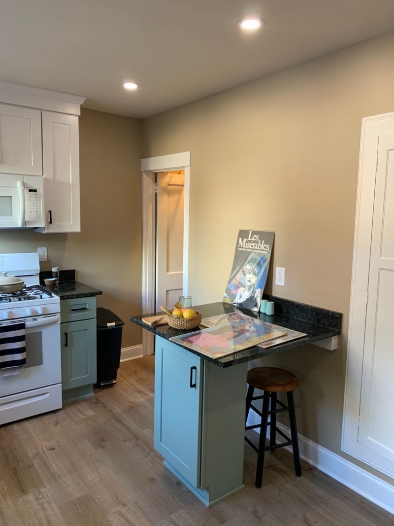 Kitchen with white cabinets, green lower cabinets, wood-look floor, island with a countertop, and a stool.