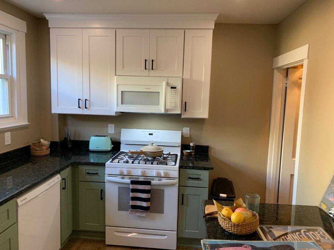 Kitchen with white upper cabinets, green lower cabinets, and dark countertops.