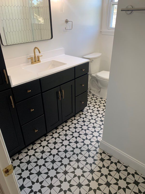 Bathroom with black vanity, white countertop, patterned floor, and gold fixtures.