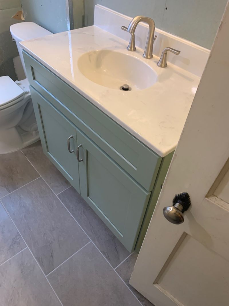 Bathroom vanity with a light green cabinet, white countertop, and gray tiled floor.