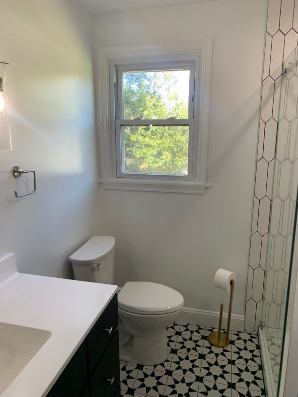Bathroom with a white toilet, black and white tiled floor, and a window overlooking greenery.