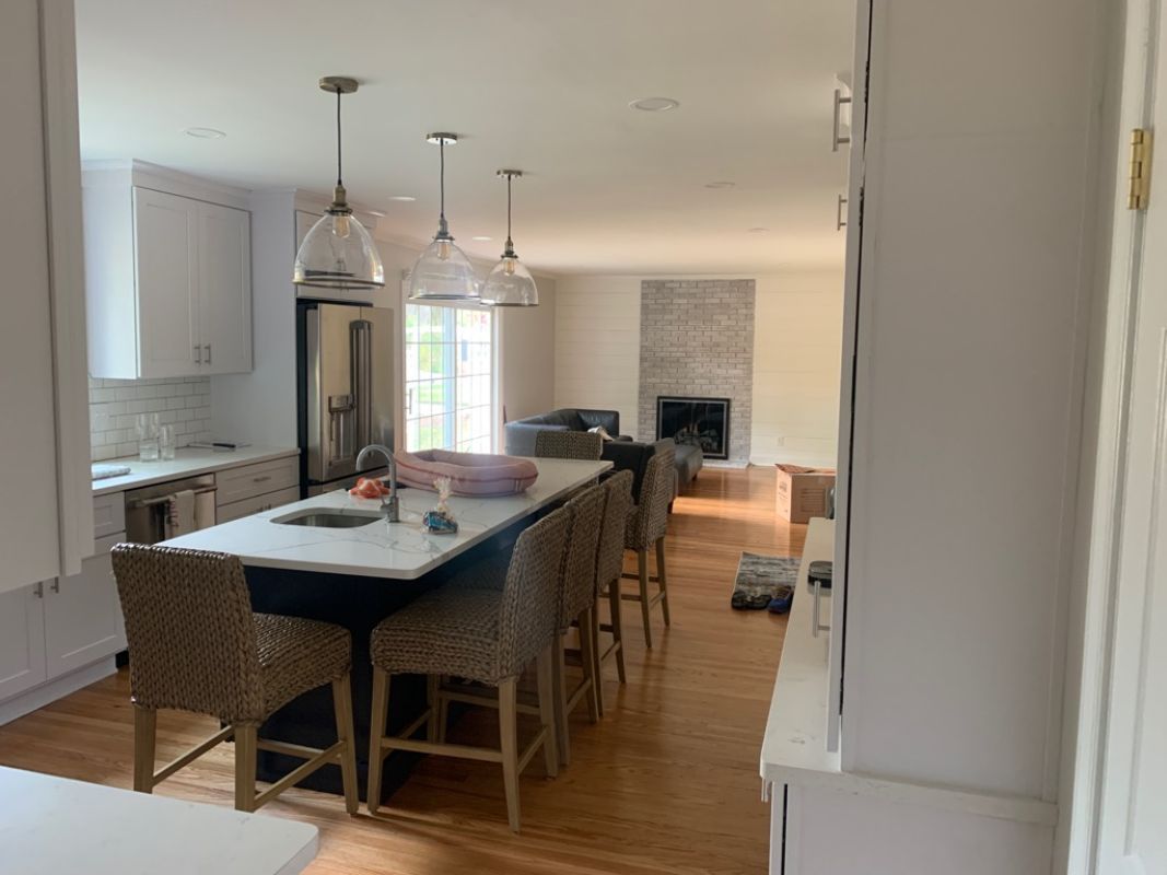 Kitchen with island and chairs, leading to a living room with a fireplace and couch.
