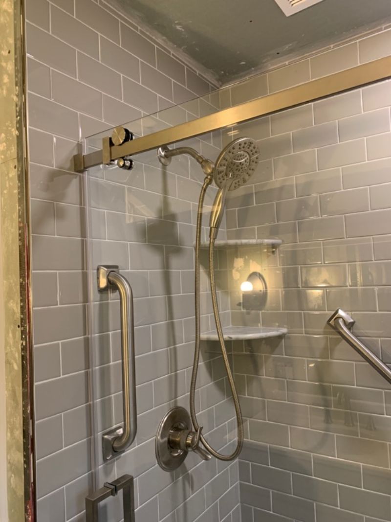 Shower with gray tile, glass door, and silver fixtures. Includes grab bars and a multi-setting shower head.