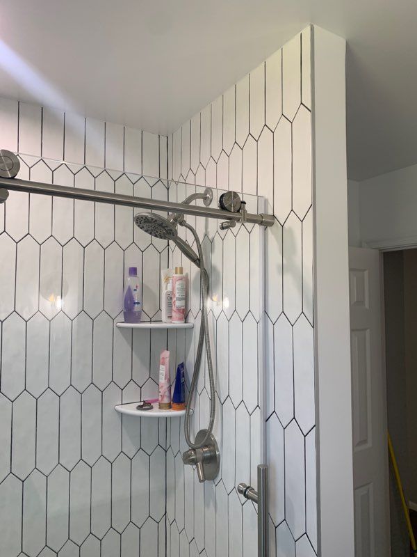 White tiled shower with a silver shower bar and head. Two shelves hold toiletries.