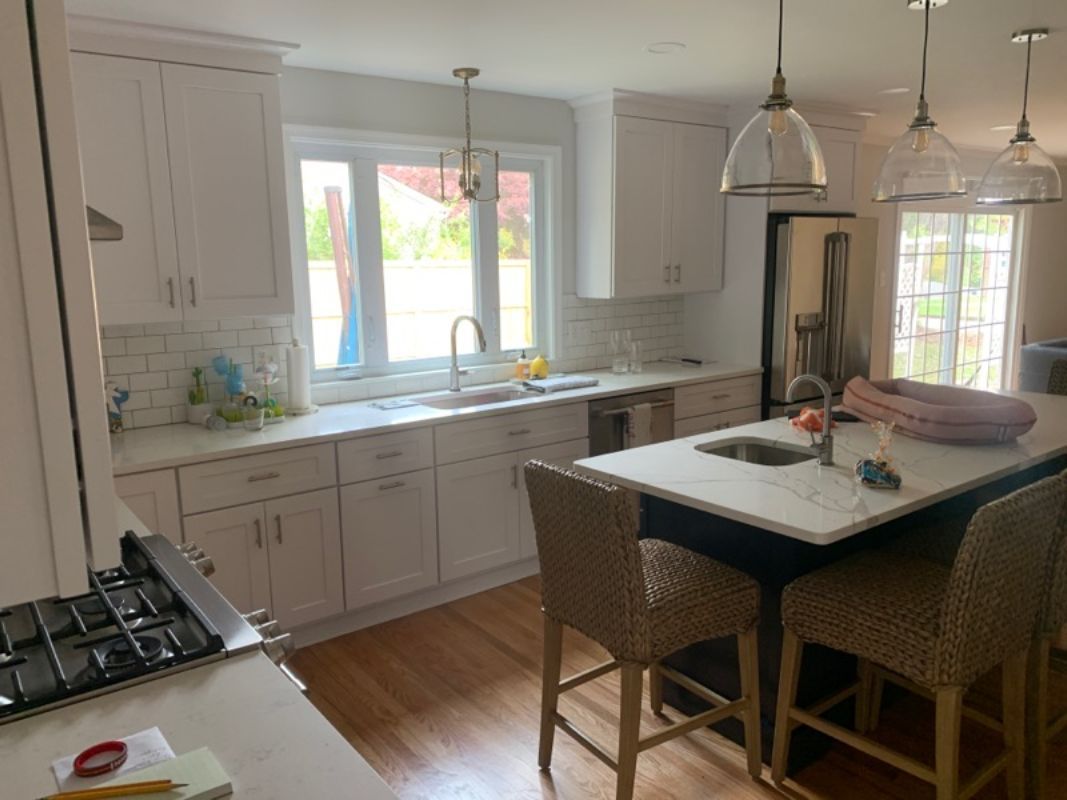 White kitchen with cabinets, island, and wood floors. Stainless steel appliances and sink by window.