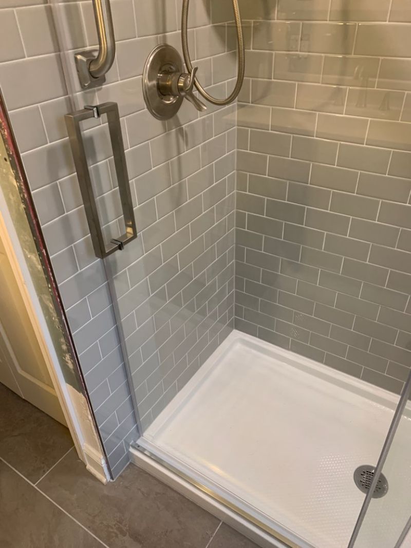A shower with gray subway tile walls and a white base, glass door and chrome fixtures.