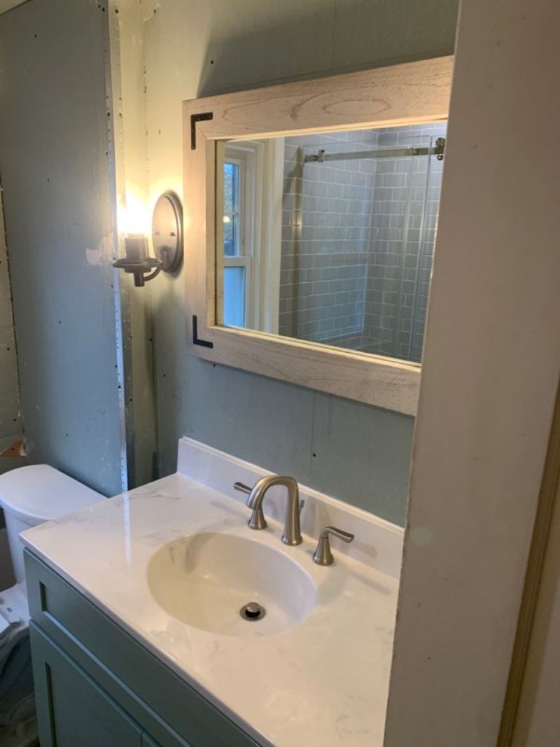 Bathroom with light blue walls, white marble countertop, vanity with a light gray wood-framed mirror.