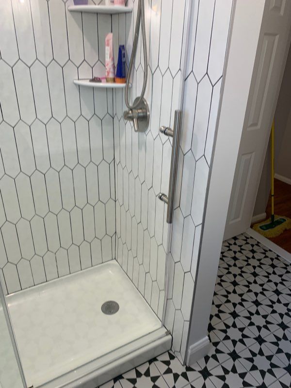 Shower with white and black tile, silver fixtures, and grab bar. Open door reveals patterned floor.