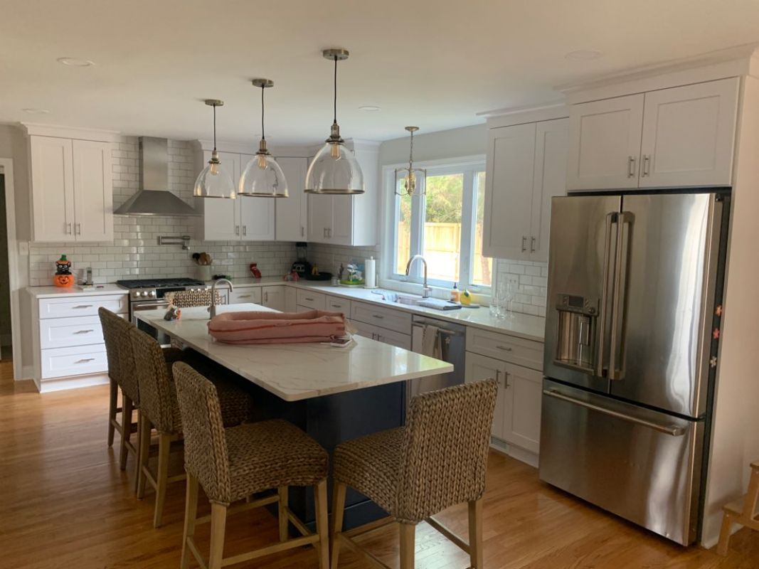 Modern white kitchen with island, stainless steel appliances, and pendant lights.