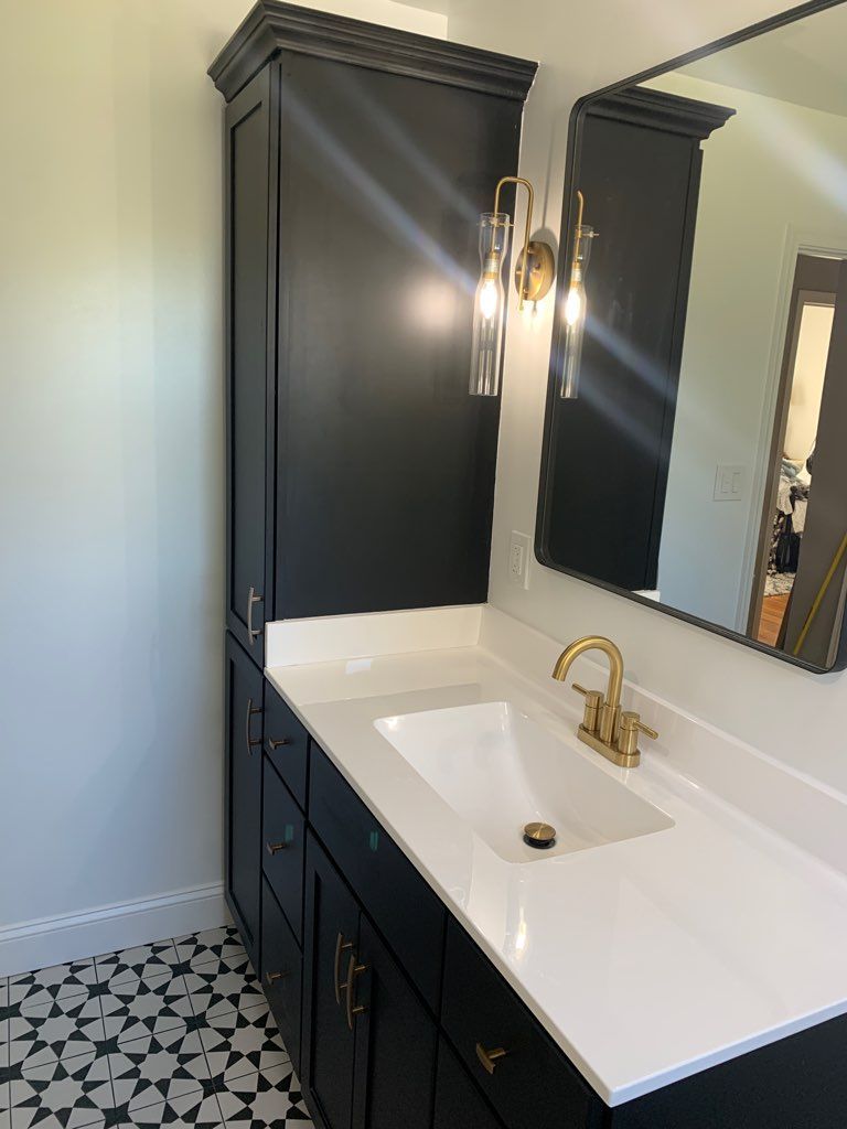 Black bathroom vanity with white countertop, gold fixtures, and a tall cabinet.