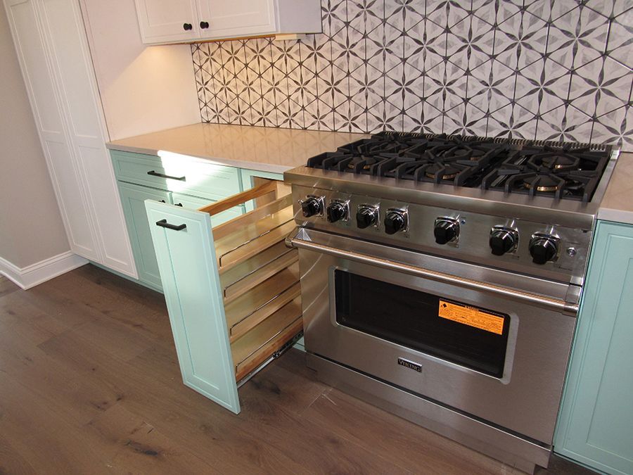 Kitchen with a stainless steel stove, pull-out storage, and patterned backsplash; light green cabinets and light countertop.