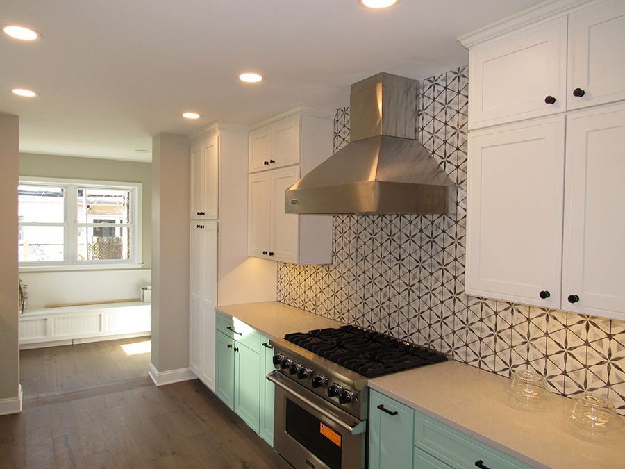 Kitchen with white cabinets, aqua lower cabinets, stainless steel range hood, and patterned backsplash.