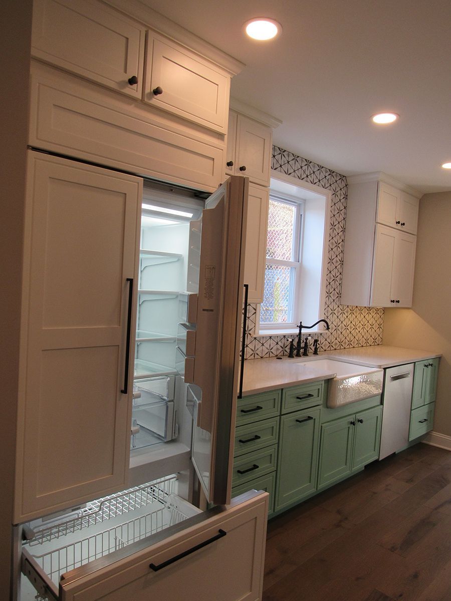 A kitchen with a partially open refrigerator. White upper cabinets, mint green lower cabinets, and a farmhouse sink.